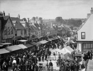 BURFORD, Oxfordshire. A view of the High Street during the Hiring Fair (Mop Fair) with stalls set out.